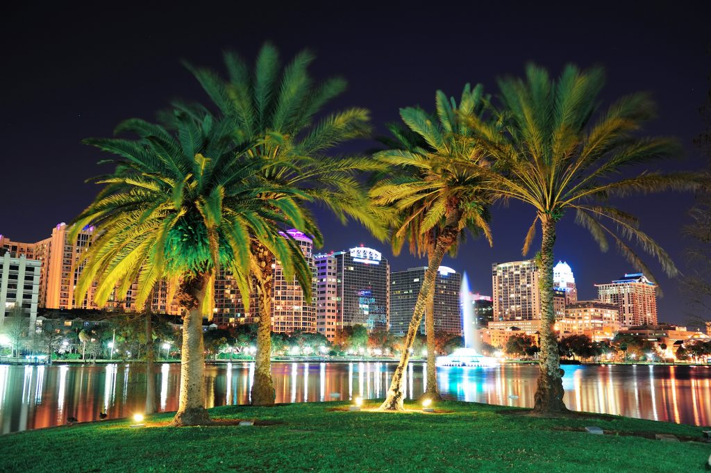 Orlando downtown skyline panorama over Lake Eola at night with urban skyscrapers, tropic palm tree a