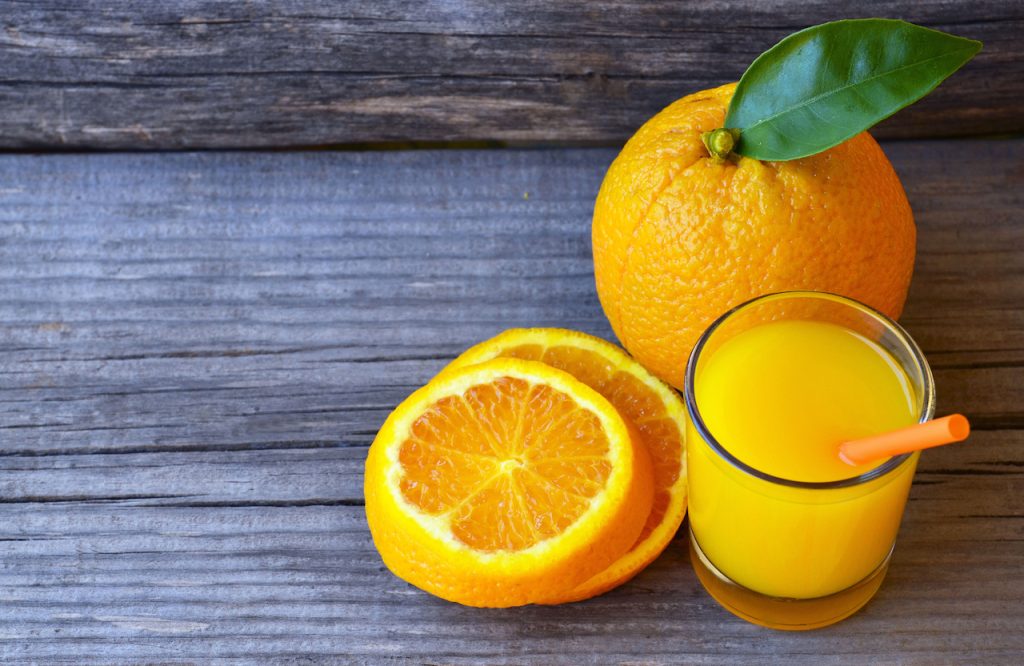 glass of fresh orange juice with a straw and fresh orange slices on a wooden background