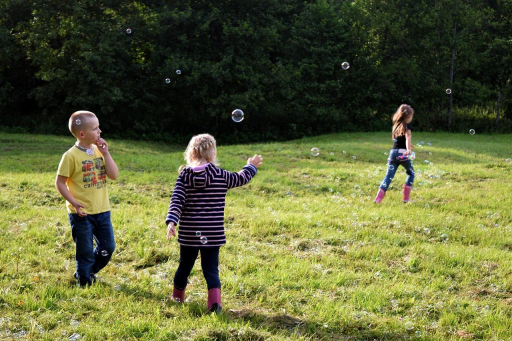 three kids in an open field playing with bubbles