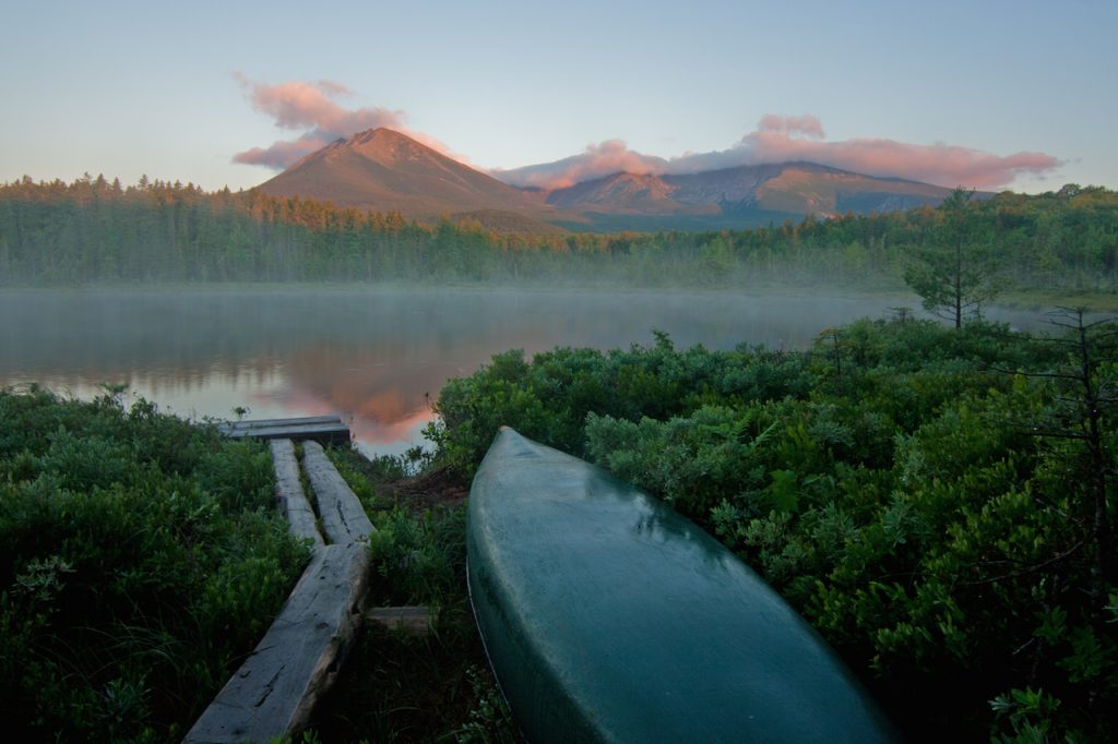 Canoe and trees on a lake in Maine. Mount Katahdin sunrise in the background.