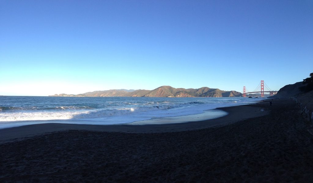 Waves and water blowing in the wind on Baker Beach with the Golden Gate Bridge in the distant background