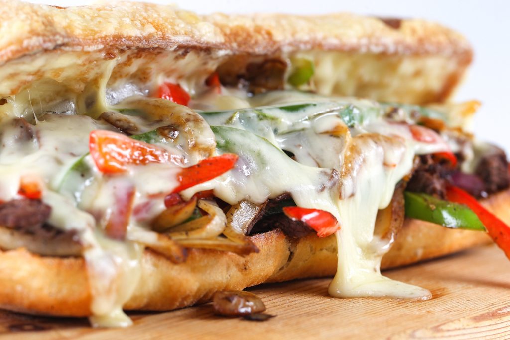 Close up of a philly cheesesteak with red and green peppers, onions, meat and cheese spilling out 