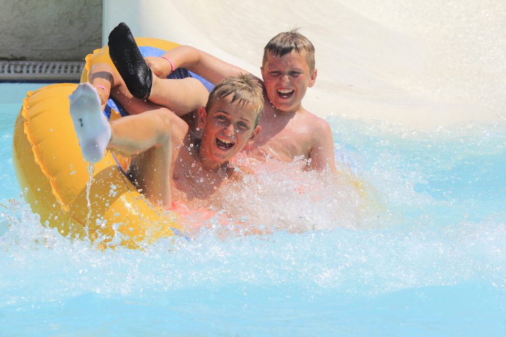 two young boys having fun in a waterpark, riding on an inner tube slide 
