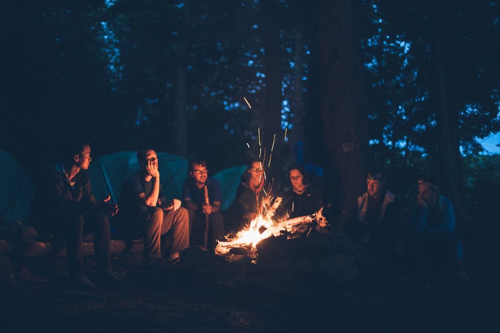 group of friends camping and sitting around a bonfire at nighttime